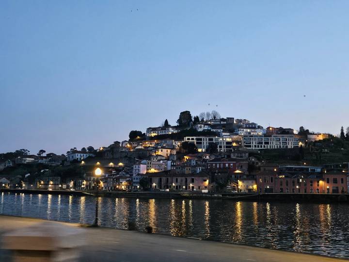 Evening lights shimmer on the water below a hillside Portuguese town just after sunset.