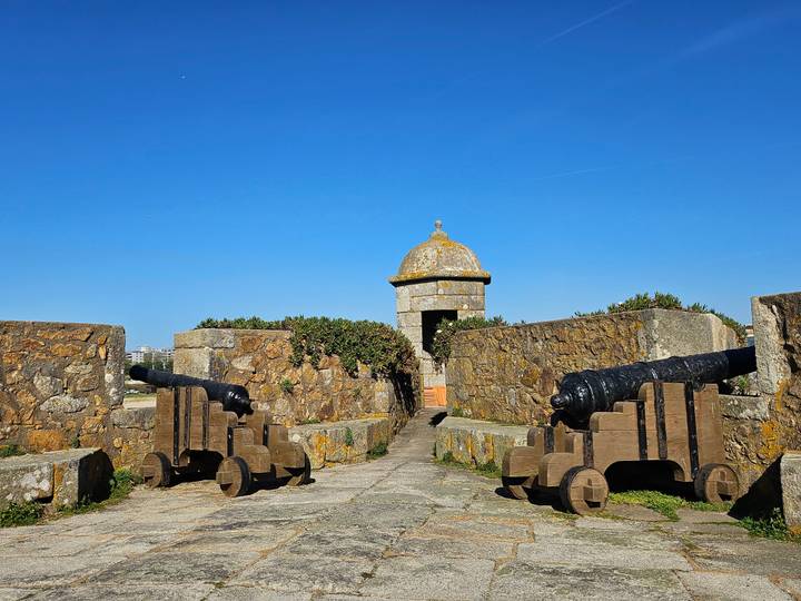 Stone fort entrance flanked by historic black cannons beneath a bright blue sky.