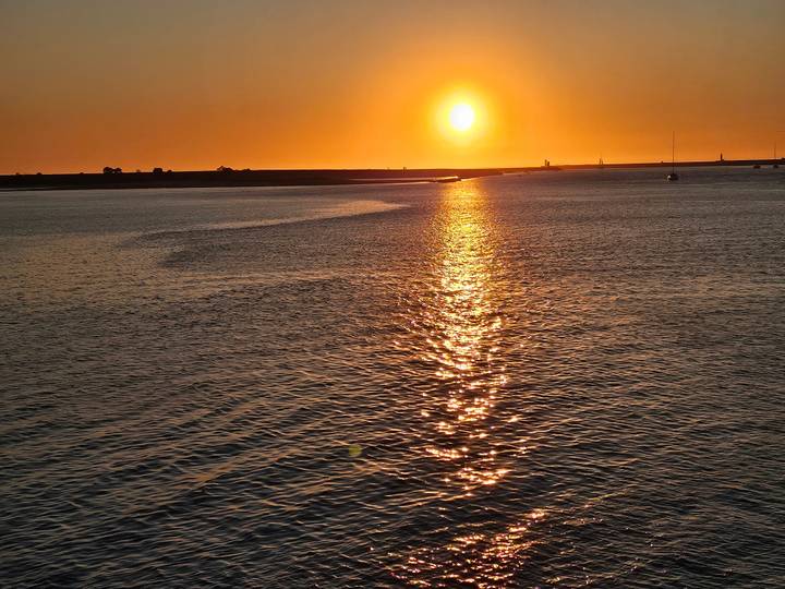 Golden sun setting over calm coastal waters leaving a shimmering reflection path.