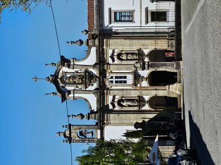 Elegant baroque church façade featuring statues and a central bell tower under clear skies.