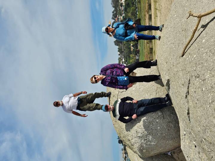 Four travellers pose on and around a large granite boulder under an overcast sky.