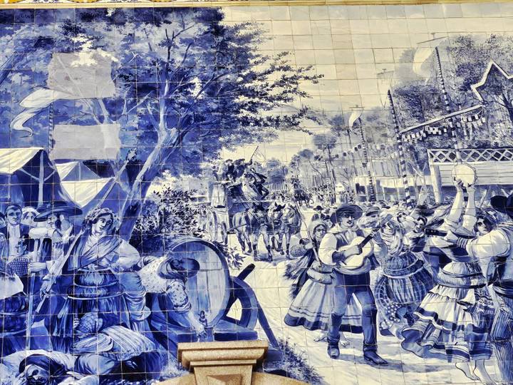 Large blue-and-white azulejo mural depicting a lively traditional Portuguese scene.