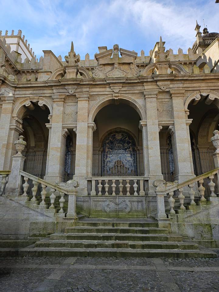 Grand stone arcade with staircases and hidden azulejo panel behind iron railings.