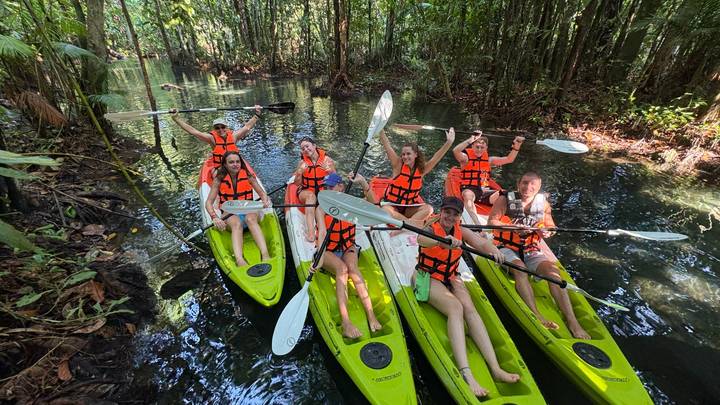 Energetic group of kayakers in bright green kayaks cheering in a narrow jungle waterway.
