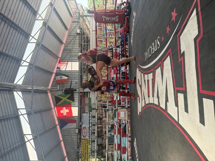 Muay Thai trainer holding pads while a student practices a high kick inside a boxing ring.