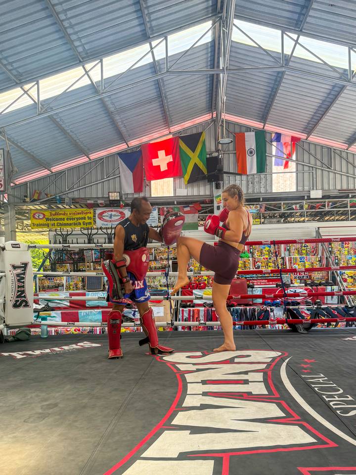 Close-up of Muay Thai sparring as a female fighter knees a pad held by her coach under national flags.
