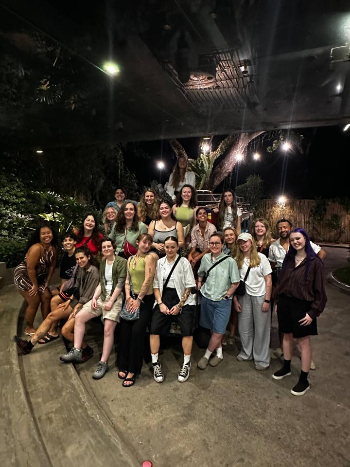 Tour group poses together at night under tree lights in a tropical courtyard.