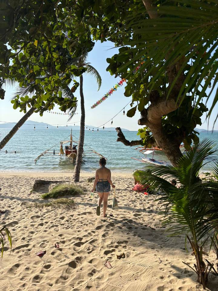 A lone traveller in swimwear gazes at outrigger boats anchored off a palm-lined shore.
