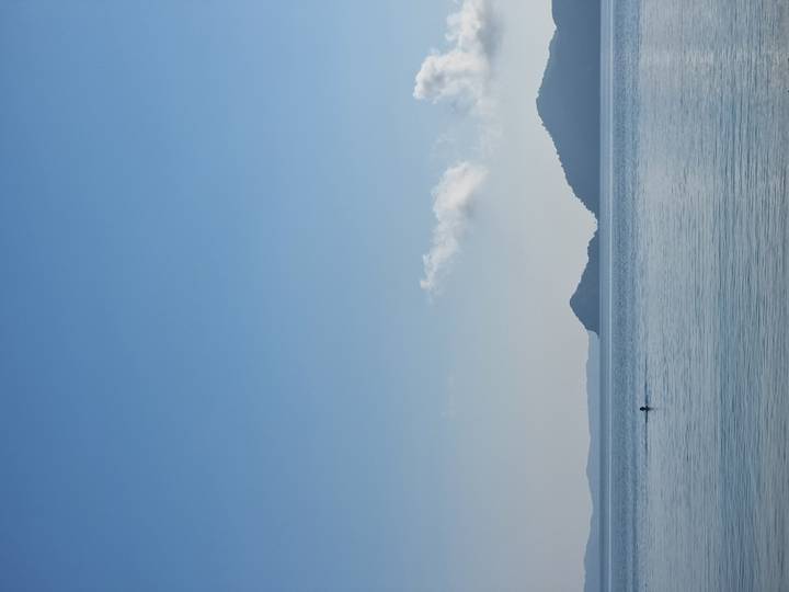 Calm blue sea with lone swimmer and distant green islands under a clear morning sky.
