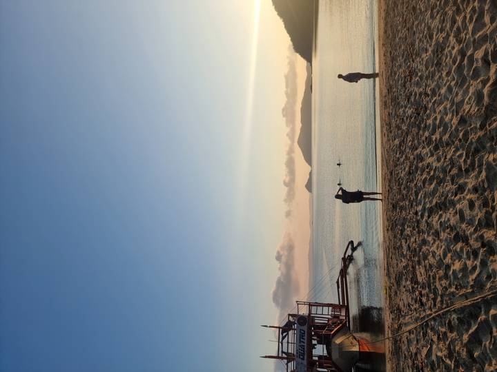 Early morning beach scene with photographers and swimmers silhouetted against soft light.