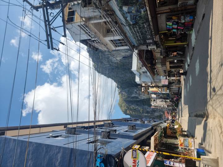 Quiet town street lined with shops beneath towering limestone cliffs and blue sky.