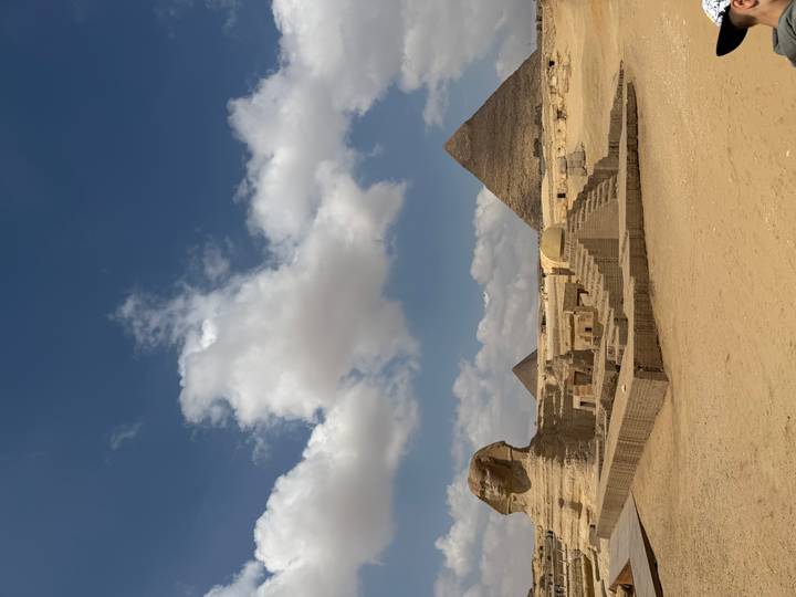 Iconic view of the Sphinx with pyramids rising behind under a blue sky dotted with clouds.