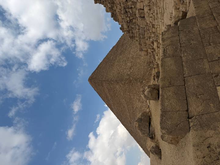 Close-up perspective of a pyramid against a dynamic sky, showing ancient stone blocks.