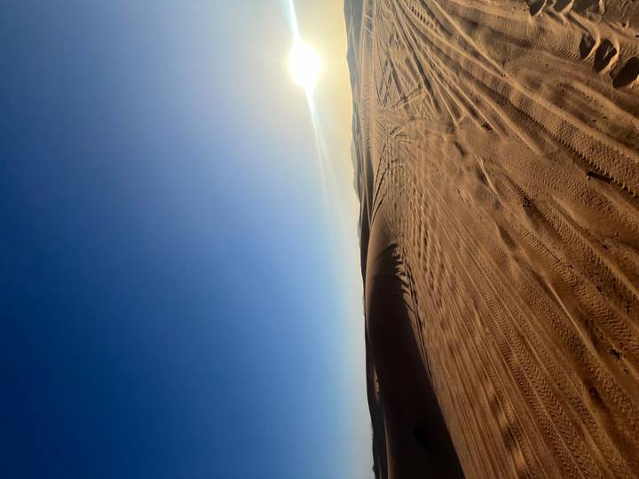 Sweeping dune landscape with tyre tracks lit by a low setting sun over distant hills.