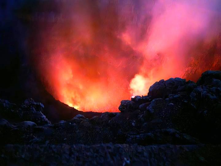 Dramatic glowing red lava illuminating the smoky interior of an active volcanic crater at night