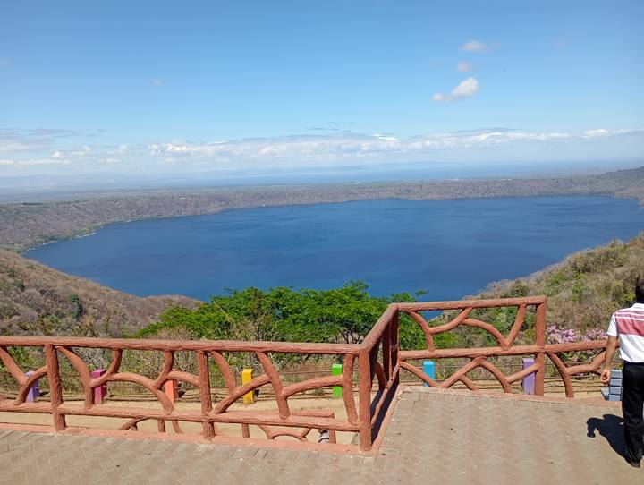 Blue volcanic crater lake viewed from a colorful wooden lookout railing on a sunny day