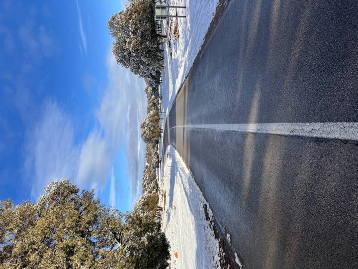 Straight snow-lined road disappearing into rolling white landscape beneath a blue sky