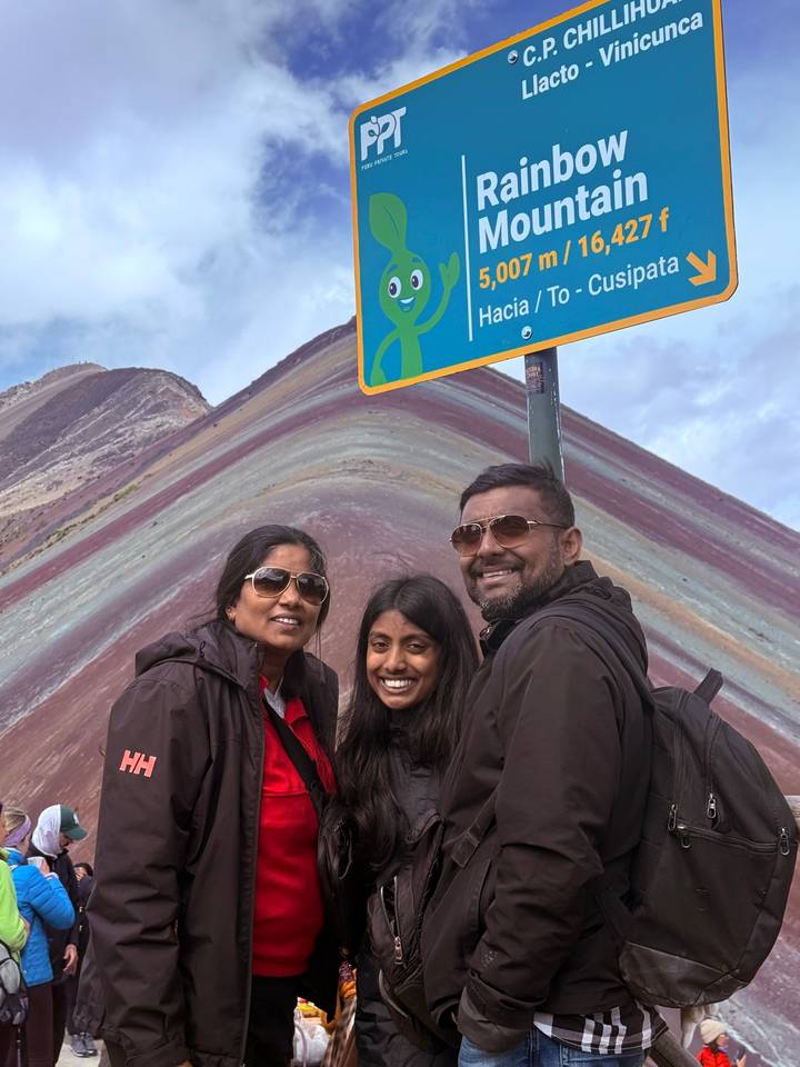 Family smiles in front of the colorful striped slopes of Rainbow Mountain in Peru.