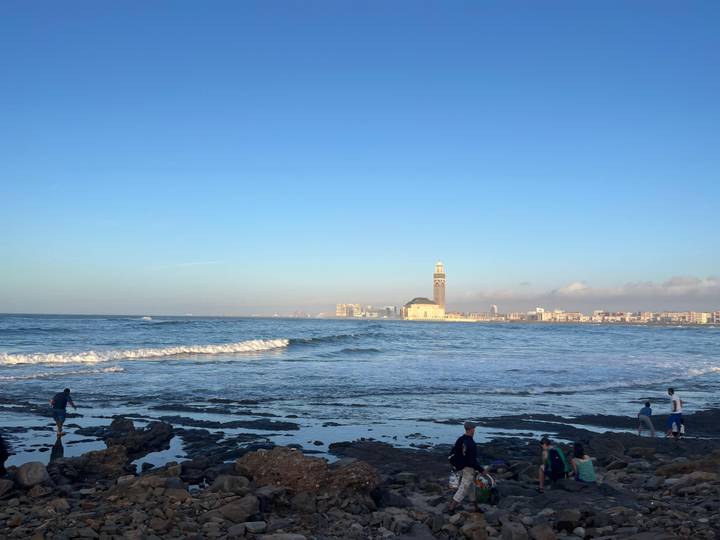 Wide coastal view with Atlantic waves and iconic Hassan II Mosque rising in background.
