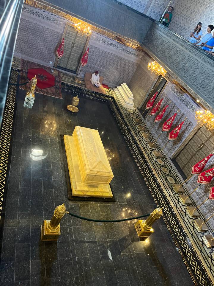 Marble sarcophagus inside an ornate mausoleum with Moroccan flags and intricate mosaics.