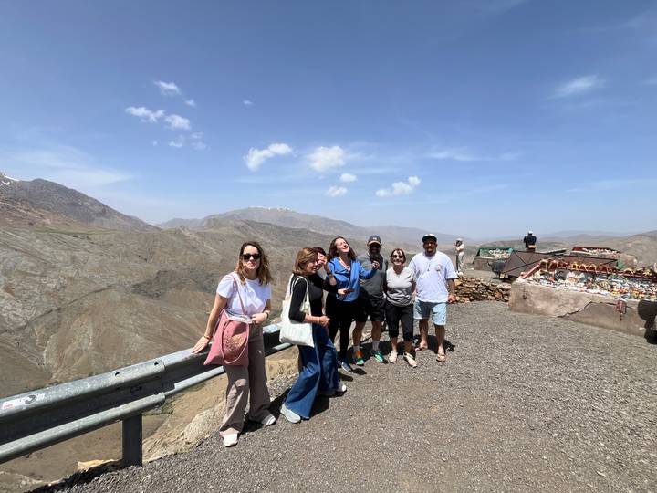 Group of travellers posing at a high mountain pass viewpoint under clear blue skies