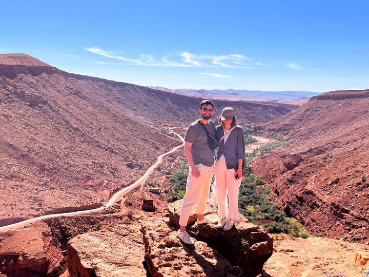Couple posing on ridge overlooking dramatic red canyon with green river oasis below