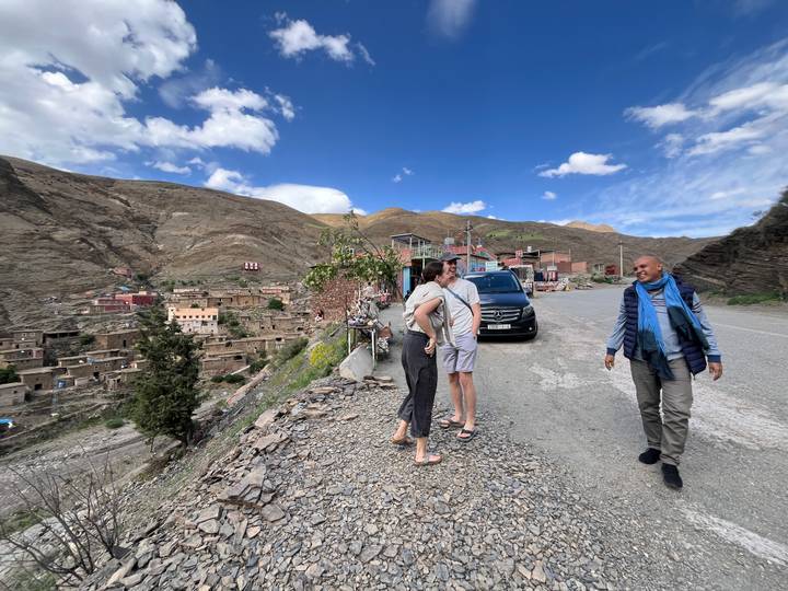 Travellers chatting beside van on roadside overlooking remote mountain village