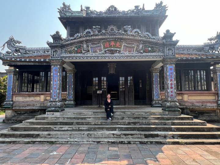 Visitor sitting on steps of an ornately decorated wooden temple building in Hue.