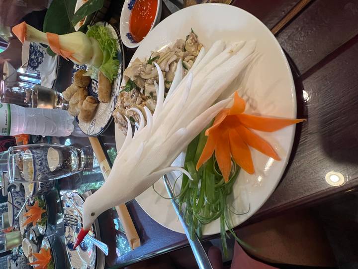 Elaborate food presentation with a carved white bird and orange flower on a Vietnamese dining table.