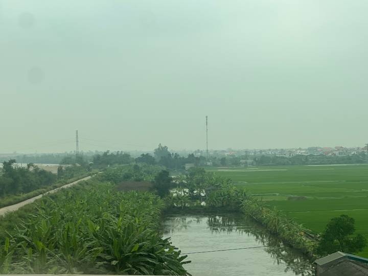 Wide view of hazy green rice fields, canals, and distant villages.