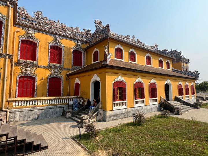 Yellow imperial residence with ornate roof and bright red shutters within Hue's citadel.
