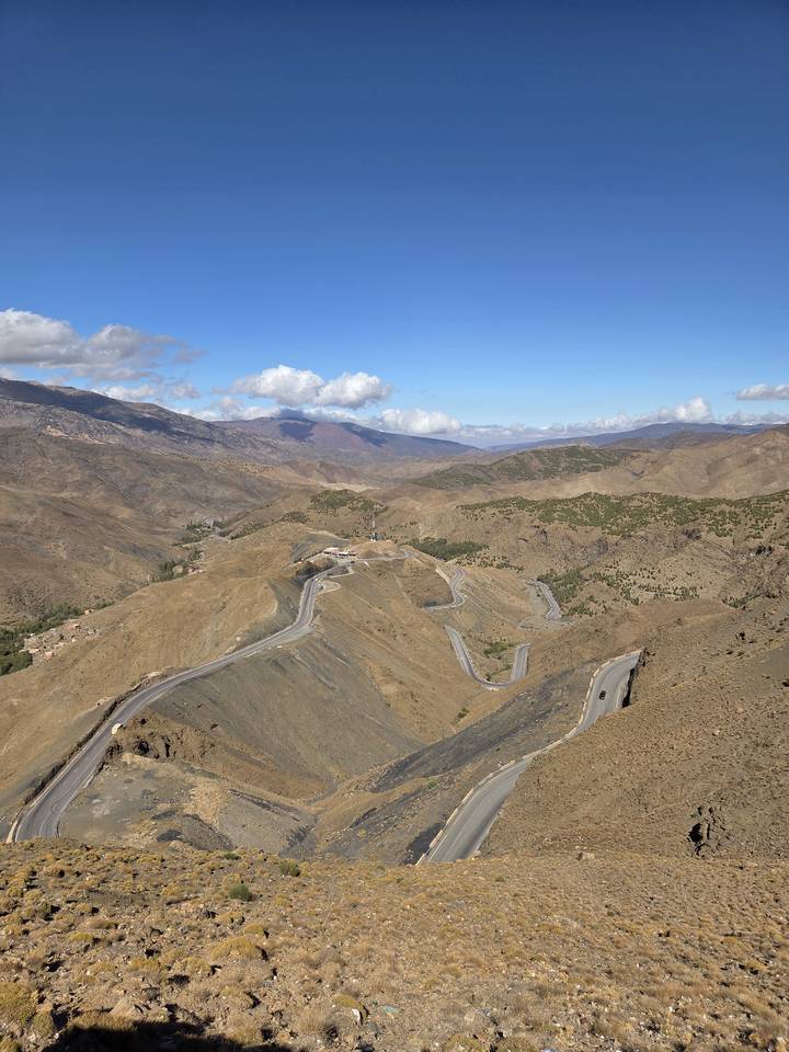 Aerial view of winding mountain road cutting through arid brown ridges under scattered clouds