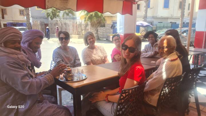 Friends and locals share tea around an outdoor café table on a sunny street