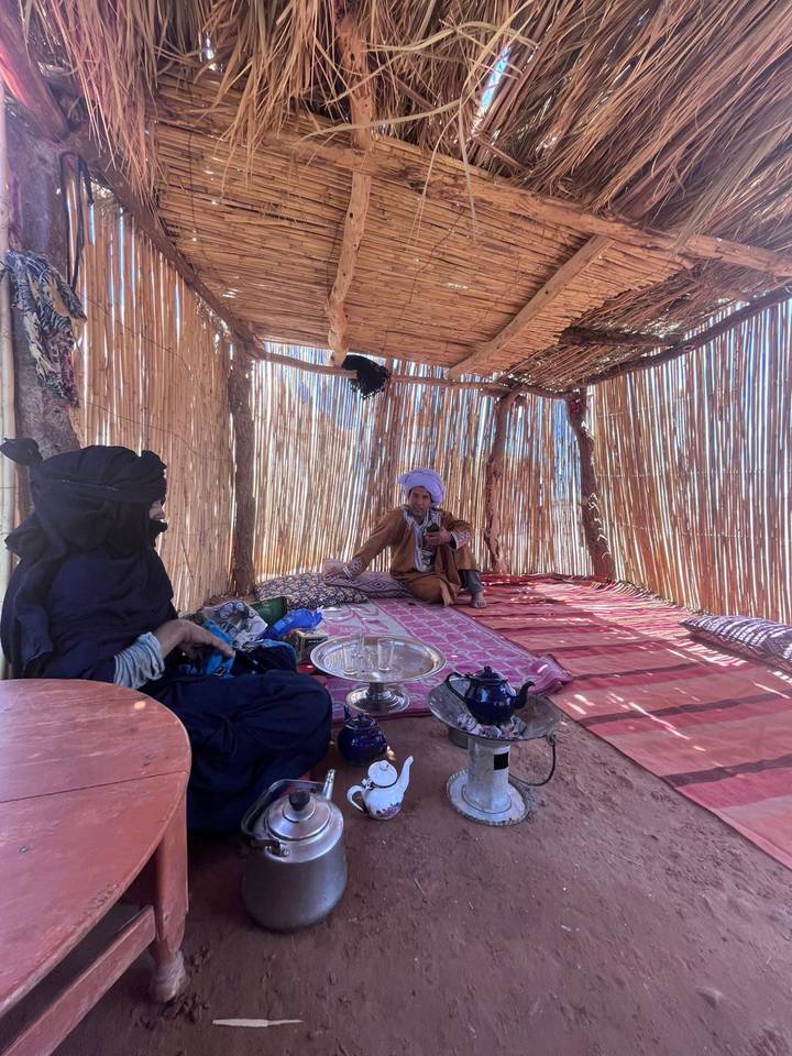 Local host pours tea for guest inside reed-walled desert shelter.