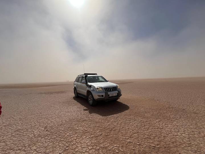 A 4x4 SUV parked on a cracked, dry lakebed with hazy desert sky creating an adventurous scene.