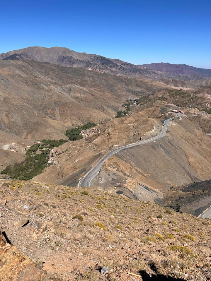 A serpentine mountain road winds through barren brown slopes with tiny villages nestled in valleys.