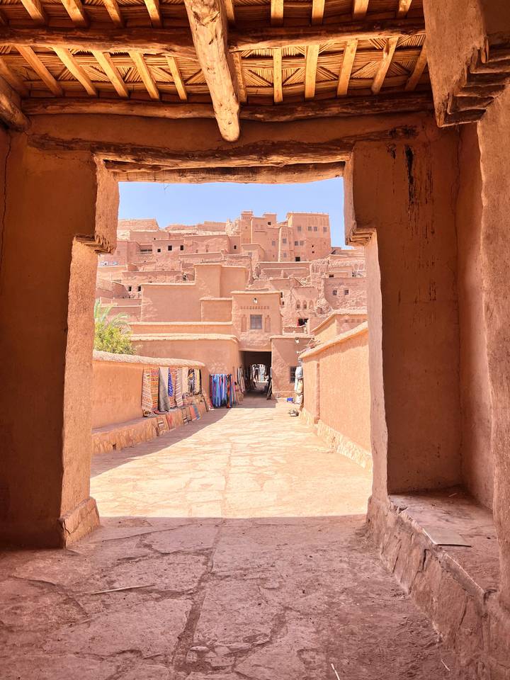 Sunlit adobe passageway lined with textiles leading into the fortified kasbah of Ait Benhaddou.