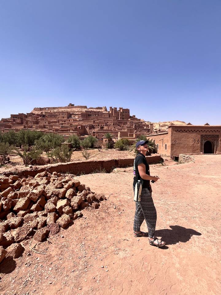 Traveller looks up at the earthen citadel of Ait Benhaddou from a sun-baked courtyard.
