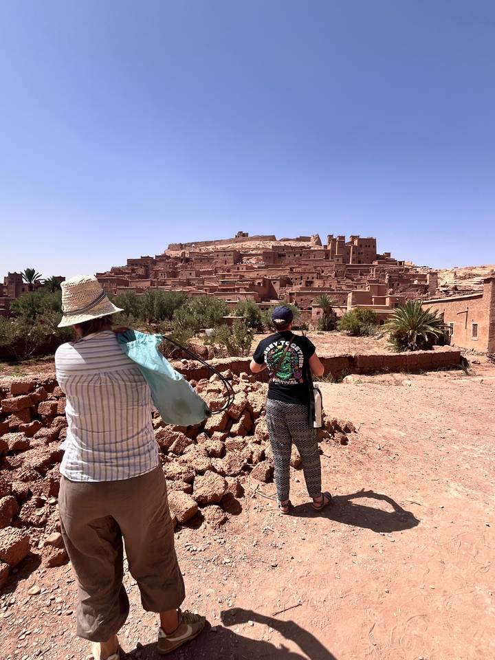 Two travellers photograph the ancient ksar of Ait Benhaddou from a nearby viewpoint.