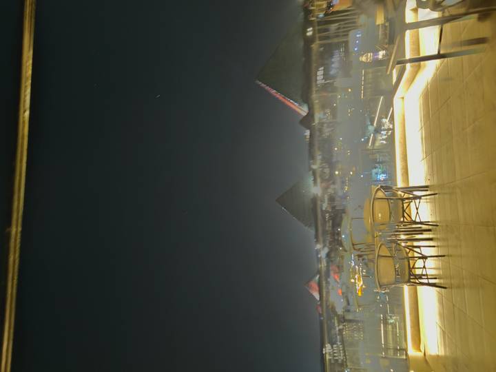Night-time rooftop view toward the softly illuminated Pyramids of Giza beyond café tables.