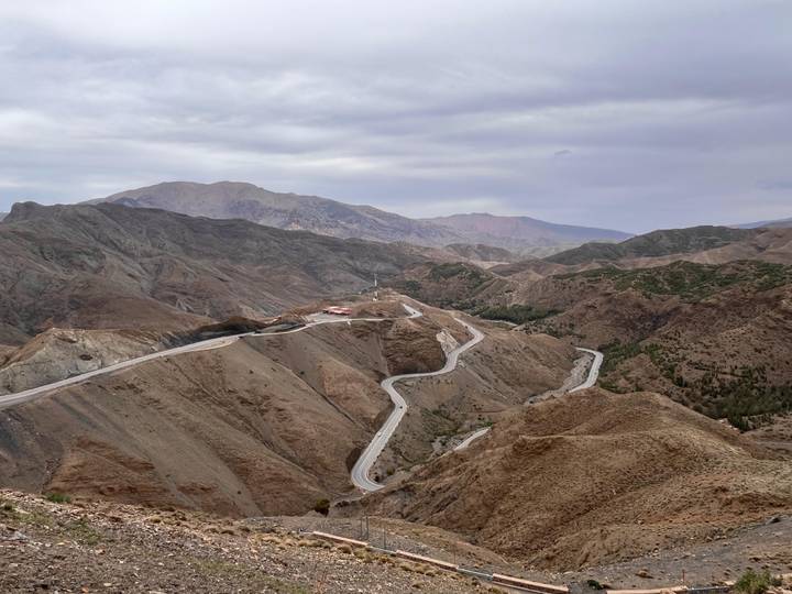 Sweeping mountain panorama with a serpentine highway snaking through barren ridges under a cloudy sky.