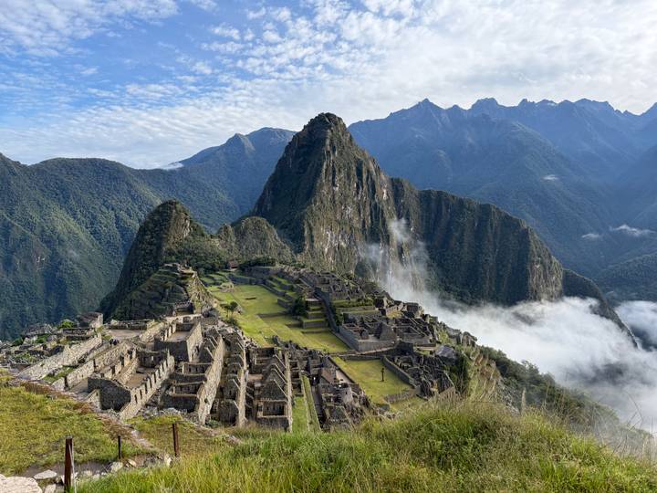 Iconic panoramic view of Machu Picchu ruins perched on a ridge with Huayna Picchu peak and drifting clouds behind.