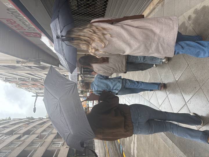Four women walk along a city street holding umbrellas on a grey, wet day.
