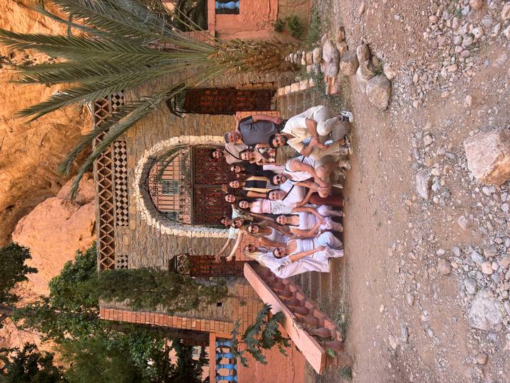Large tour group poses on stone steps before an ornate gate set into a cliffside.