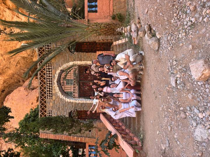 Repeat shot of the travel group smiling on the stone staircase with palm and cliff backdrop.