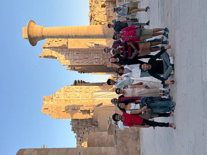 Tour group poses in front of towering sandstone columns and ruins of Karnak Temple at sunset.