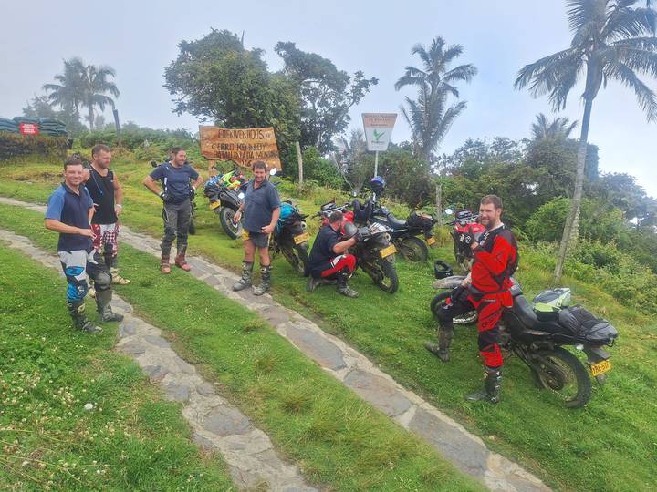 Motorbike riders in full gear pause at a mountain viewpoint beside their dual-sport bikes.