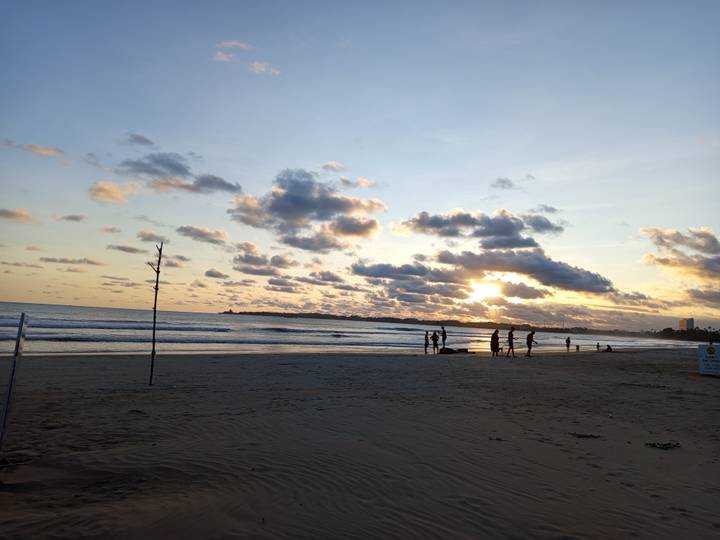 Silhouettes of beachgoers enjoy sunset on a wide sandy shore under cloud-streaked skies.
