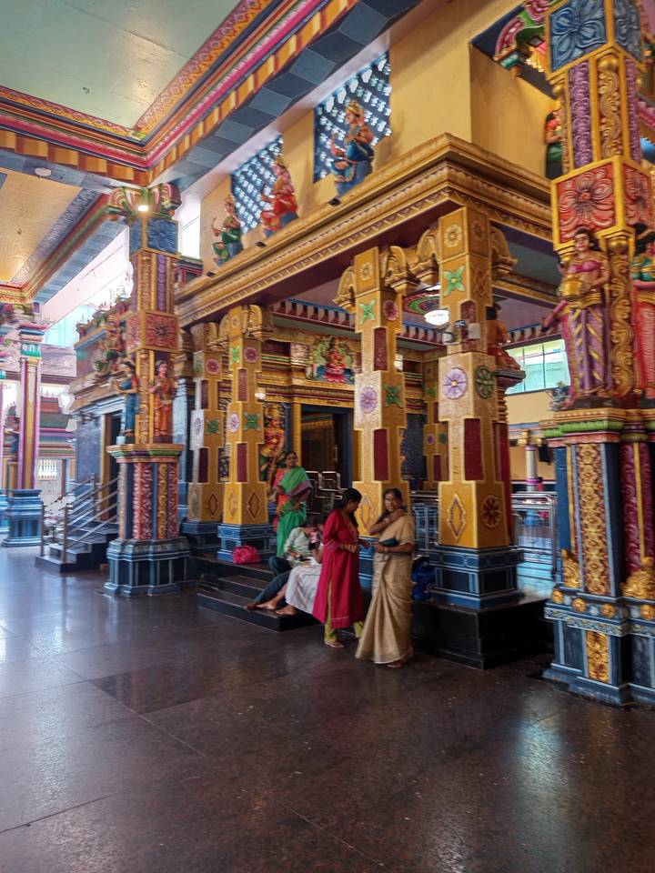 Vividly painted pillars and locals in traditional dress inside a colourful Sri Lankan Hindu temple.