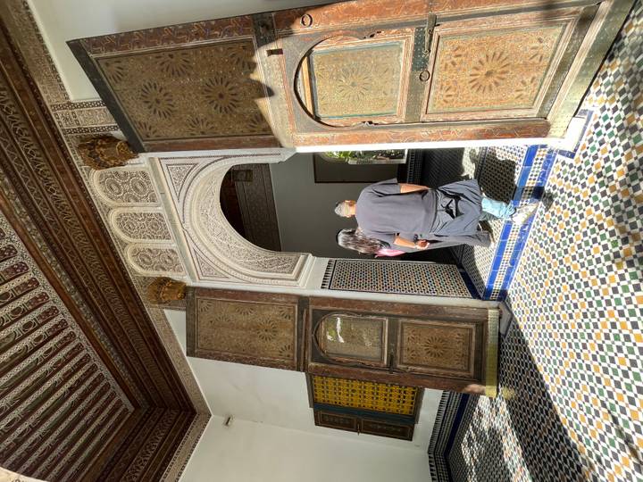 A couple steps through ornate wooden doors into a mosaic-floored hall with carved plaster arches.